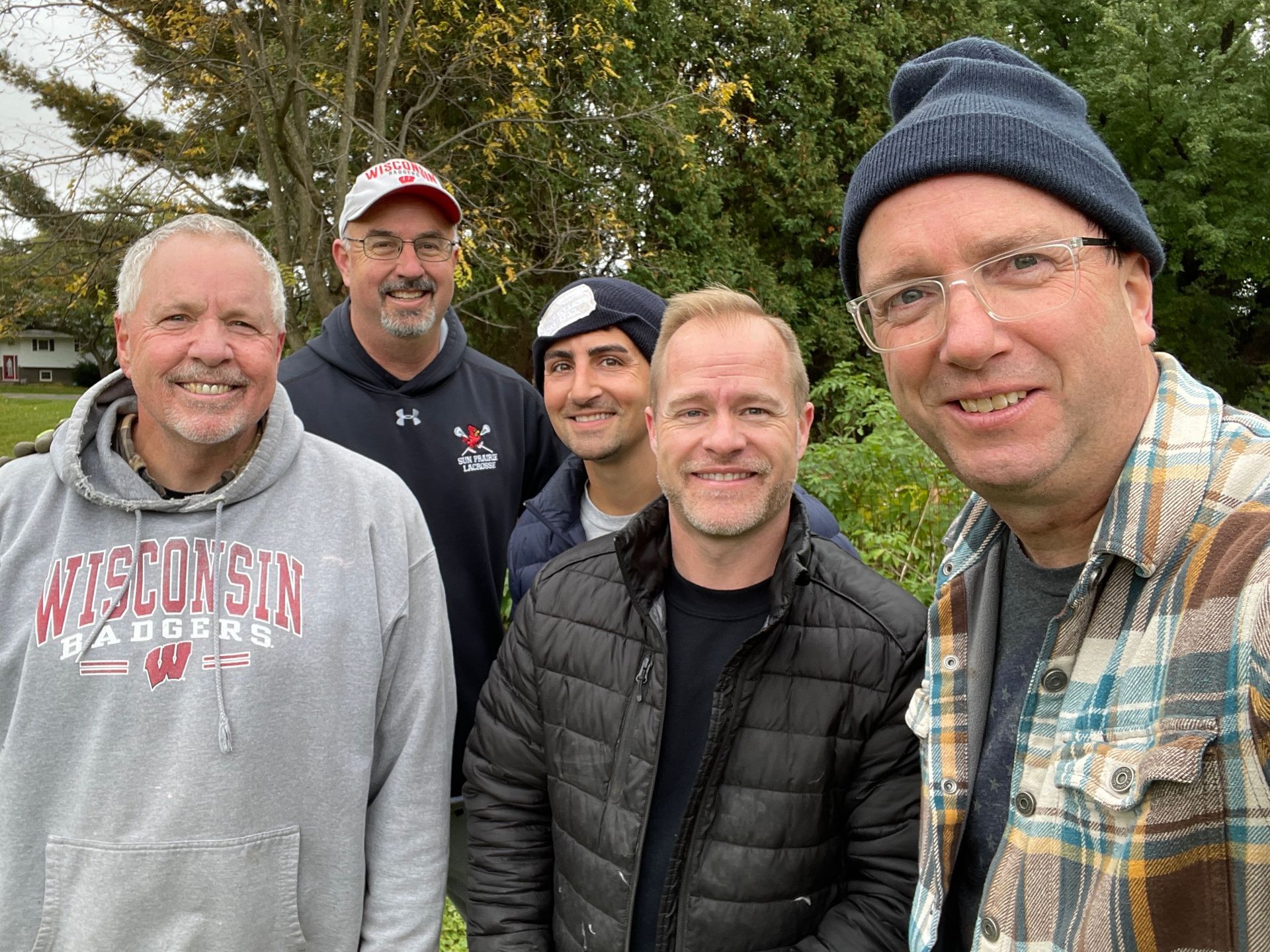 A group of men are posing for a picture together . one of the men is wearing a wisconsin raiders shirt.