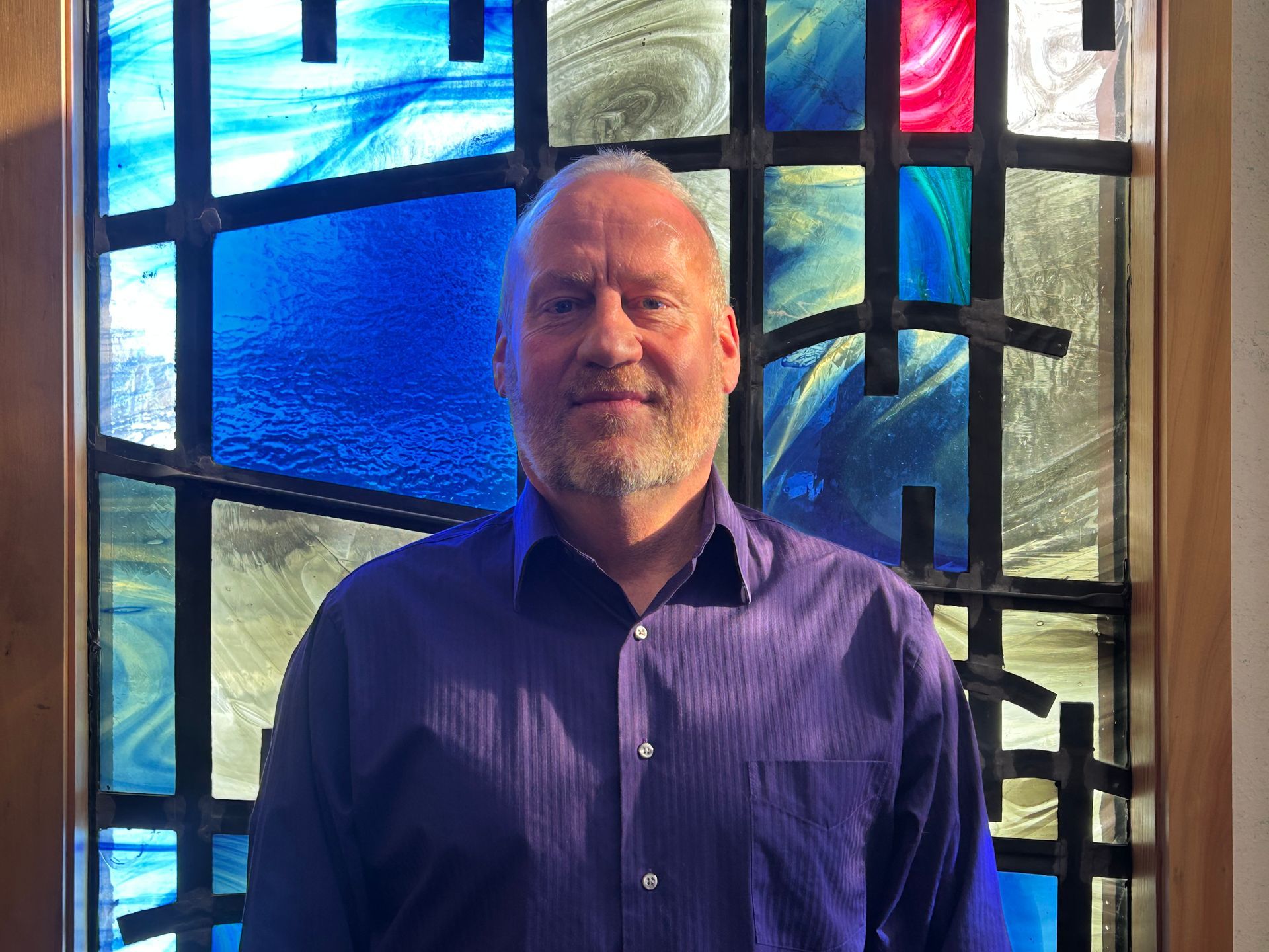 A woman is smiling in front of a stained glass window