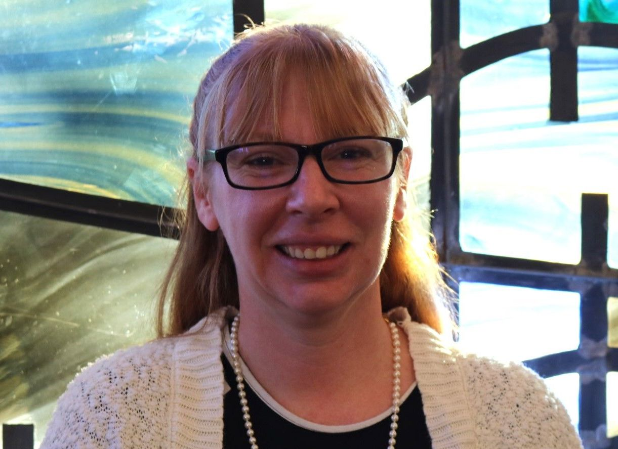 A woman wearing glasses and a pearl necklace smiles for the camera
