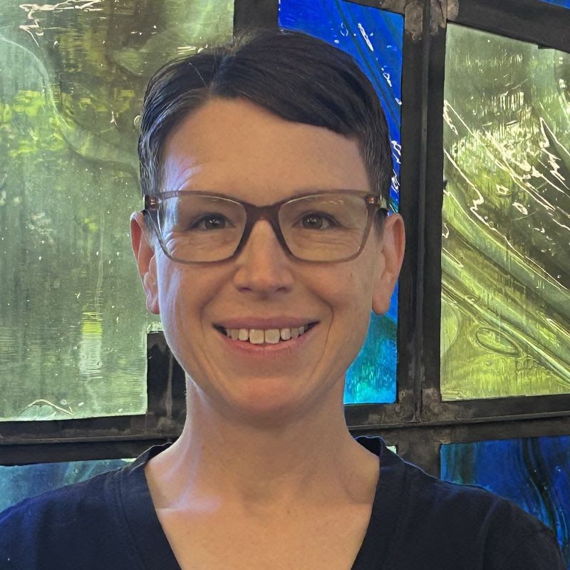 A woman is smiling in front of a stained glass window.