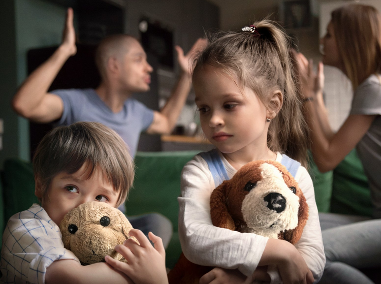 A little girl is holding a stuffed dog while her parents argue in the background.