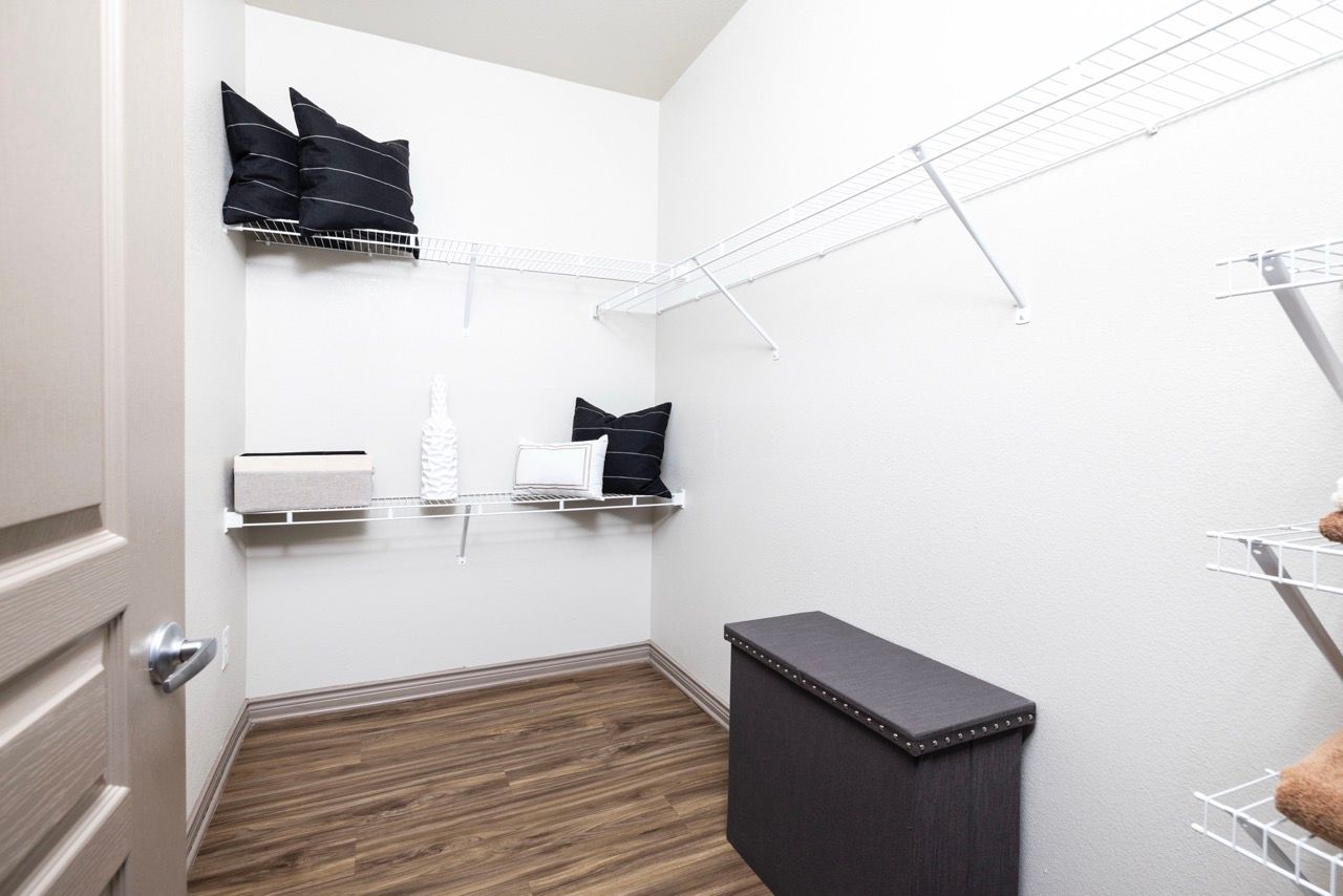 Interior walk-in closet with white wire shelving, a dark bench, and decorative pillows.