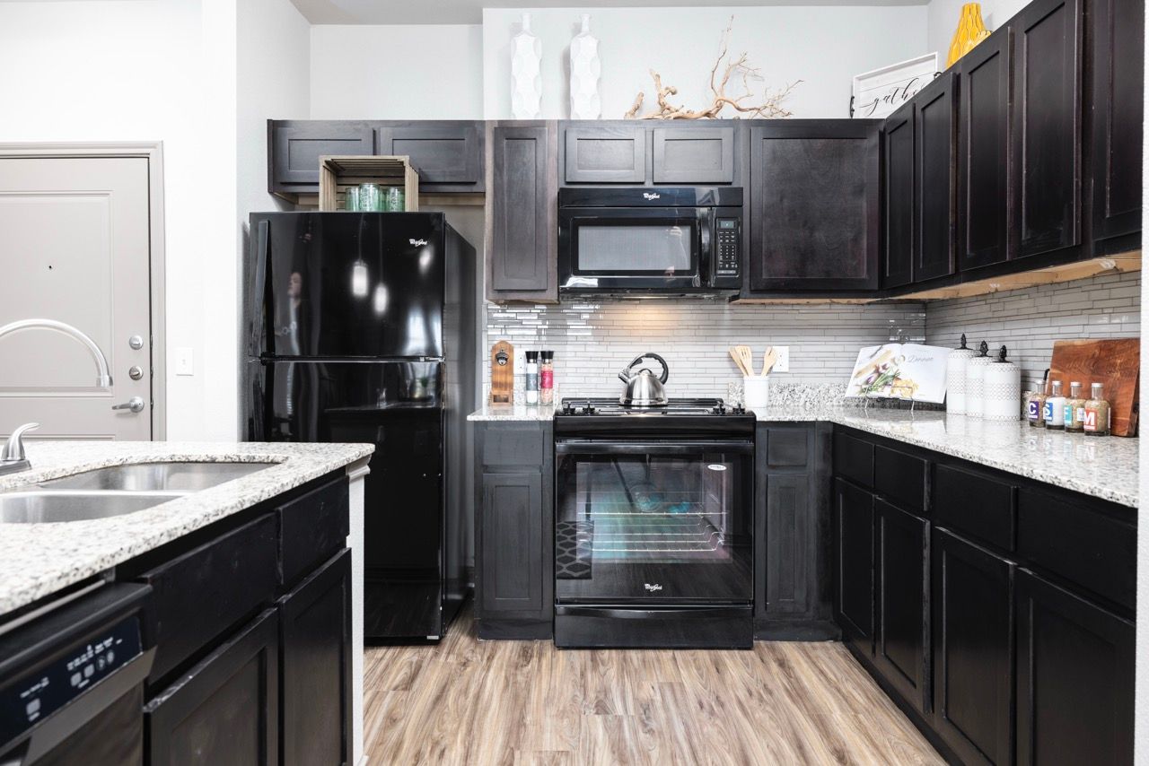 Modern kitchen in a dark-toned apartment with black appliances, granite countertops, and wood-look flooring.