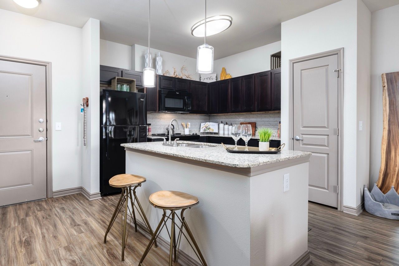 Open-concept kitchen with granite island, black appliances, and two bar stools.