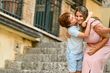 Boy kissing woman's cheek, both smiling. Stone steps in background.