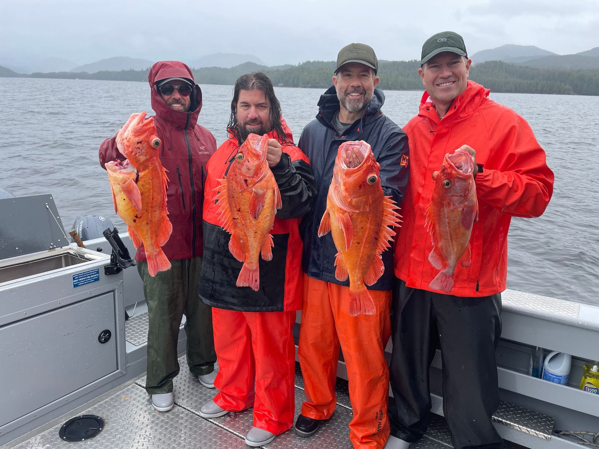 Four people on a boat display large, orange fish. Cloudy day; coastal background.