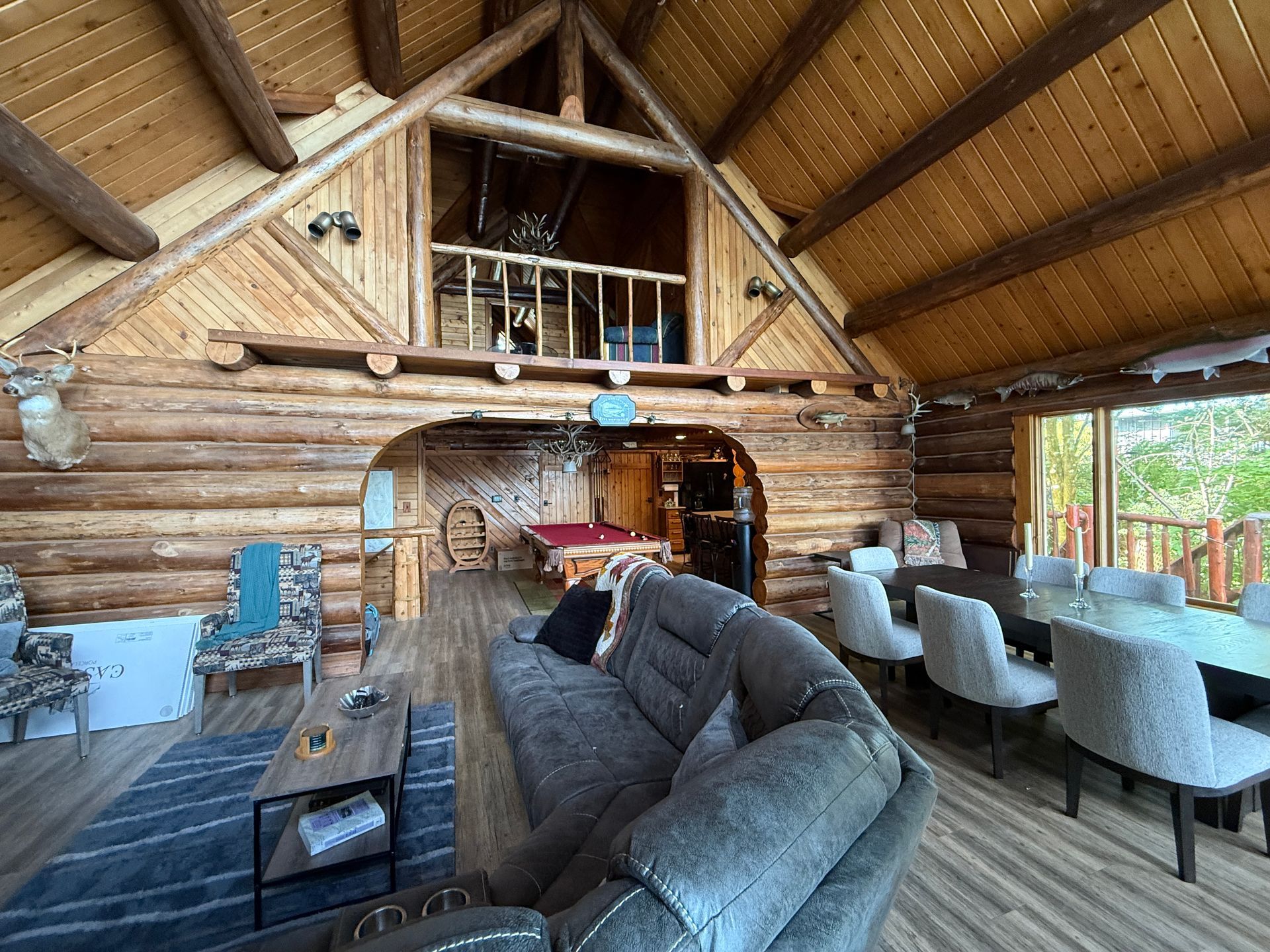 Interior of a log cabin with high ceilings. A sofa faces a pool table, and a dining table is set for a meal.
