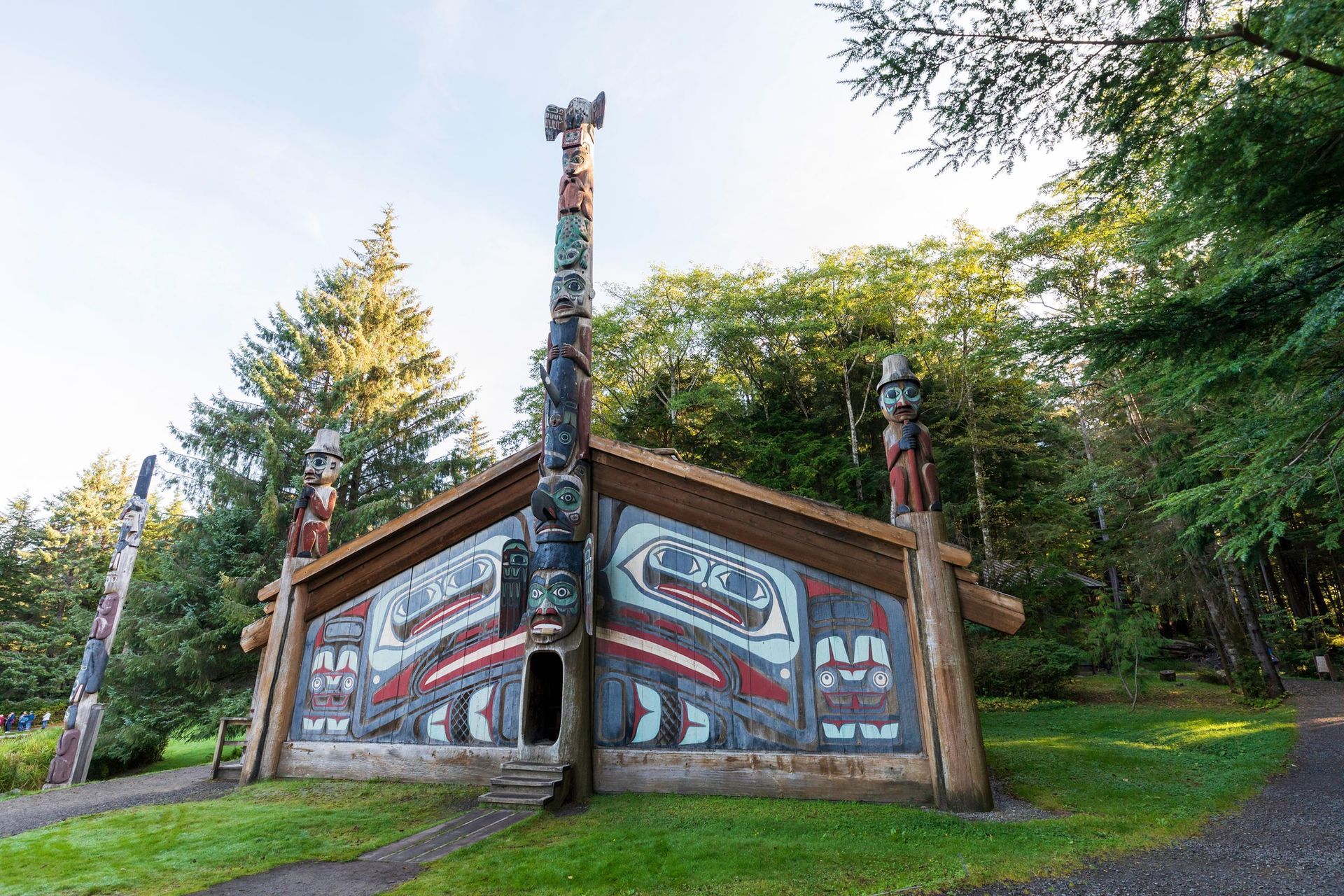 A Native American tribal house with totem poles and colorful carvings against a backdrop of trees.
