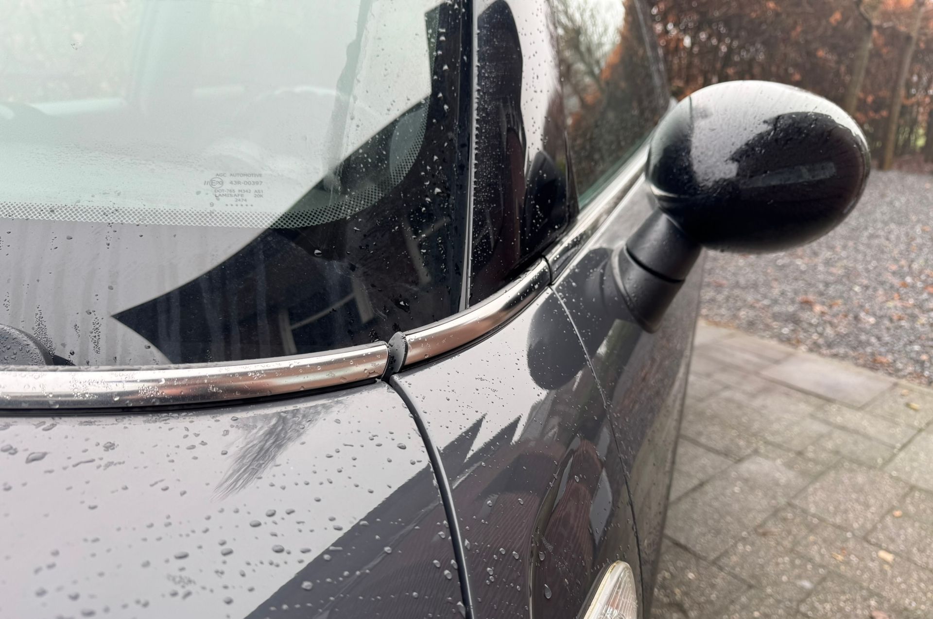 Een close-up van de zijspiegel en voorruit van een zwarte auto met een chromen rand langs het raam.