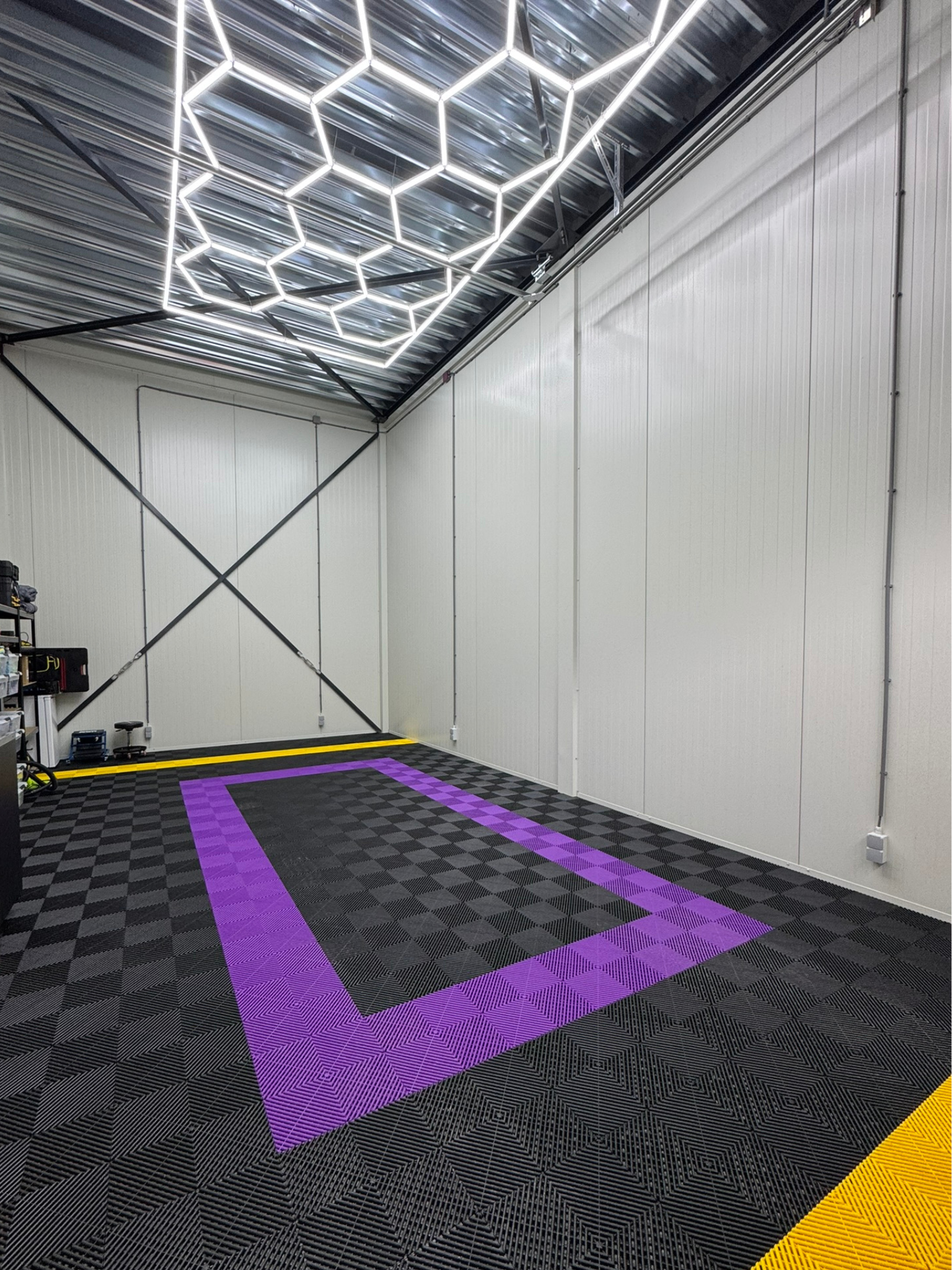 Lege autowasruimte met honingraatverlichting, geblokte vloer met paarse rechthoek, witte muren.