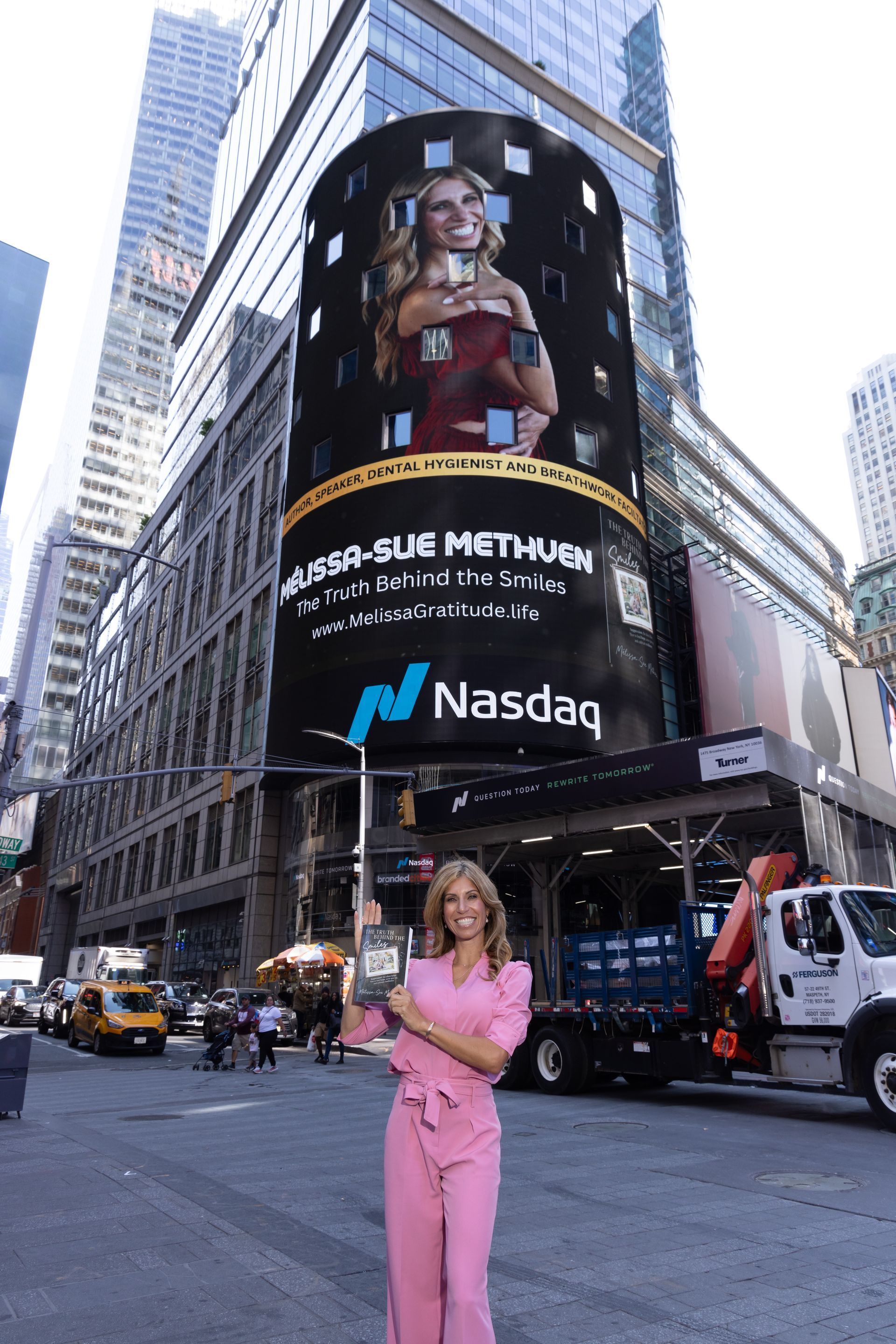 Woman in pink jumpsuit in front of the NASDAQ building in NYC, billboard features a woman.