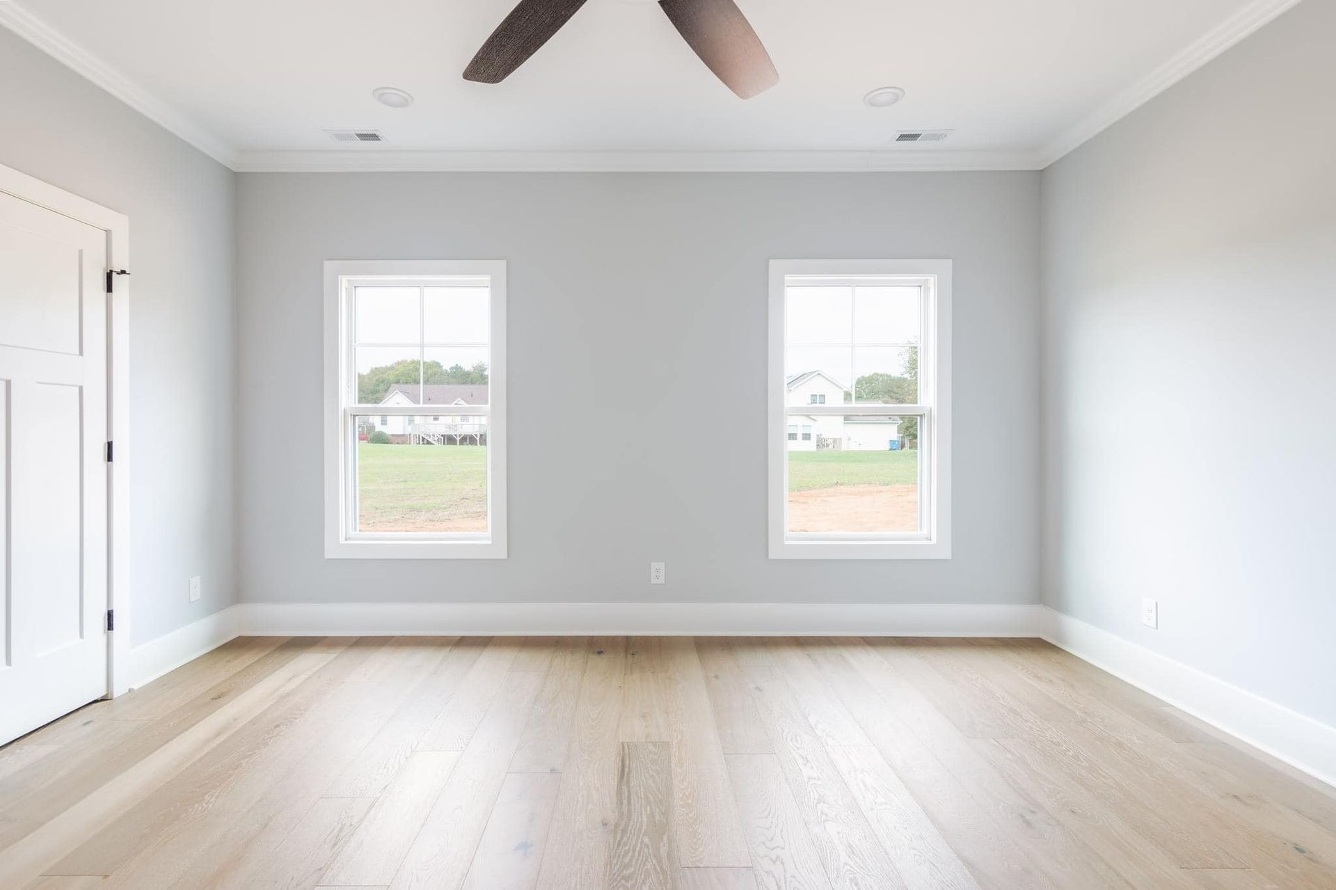 An empty room with two windows and a ceiling fan.
