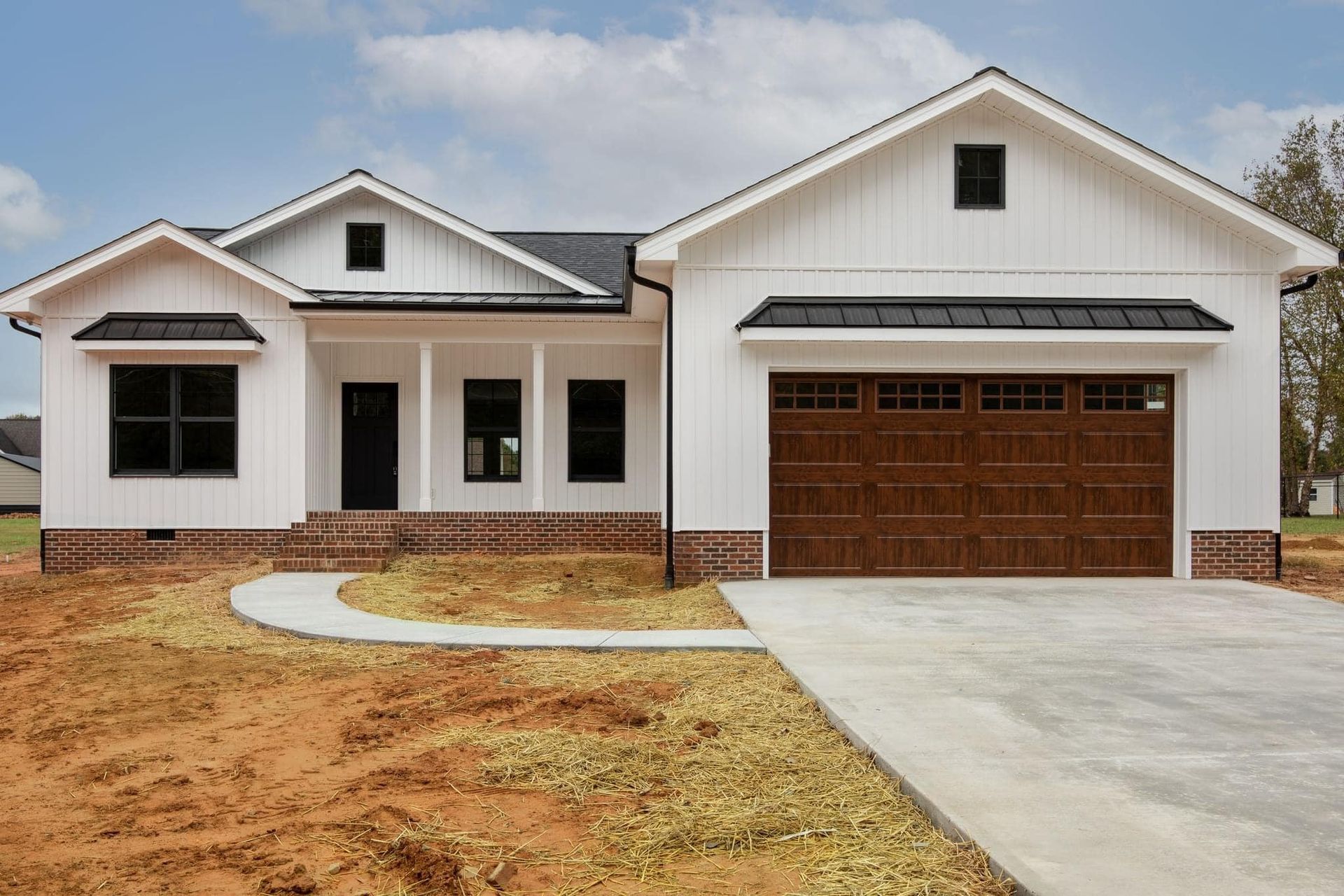 A white house with a brown garage door is sitting on top of a dirt field.