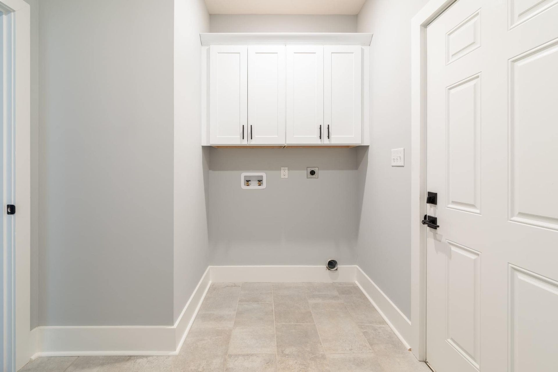 An empty laundry room with white cabinets and a door.