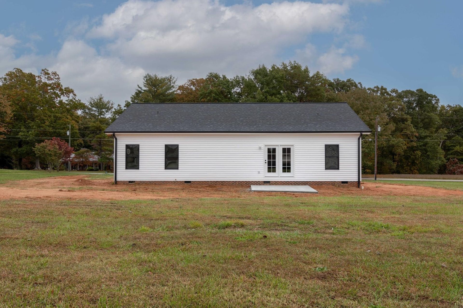 A white house with a black roof is sitting in the middle of a grassy field.