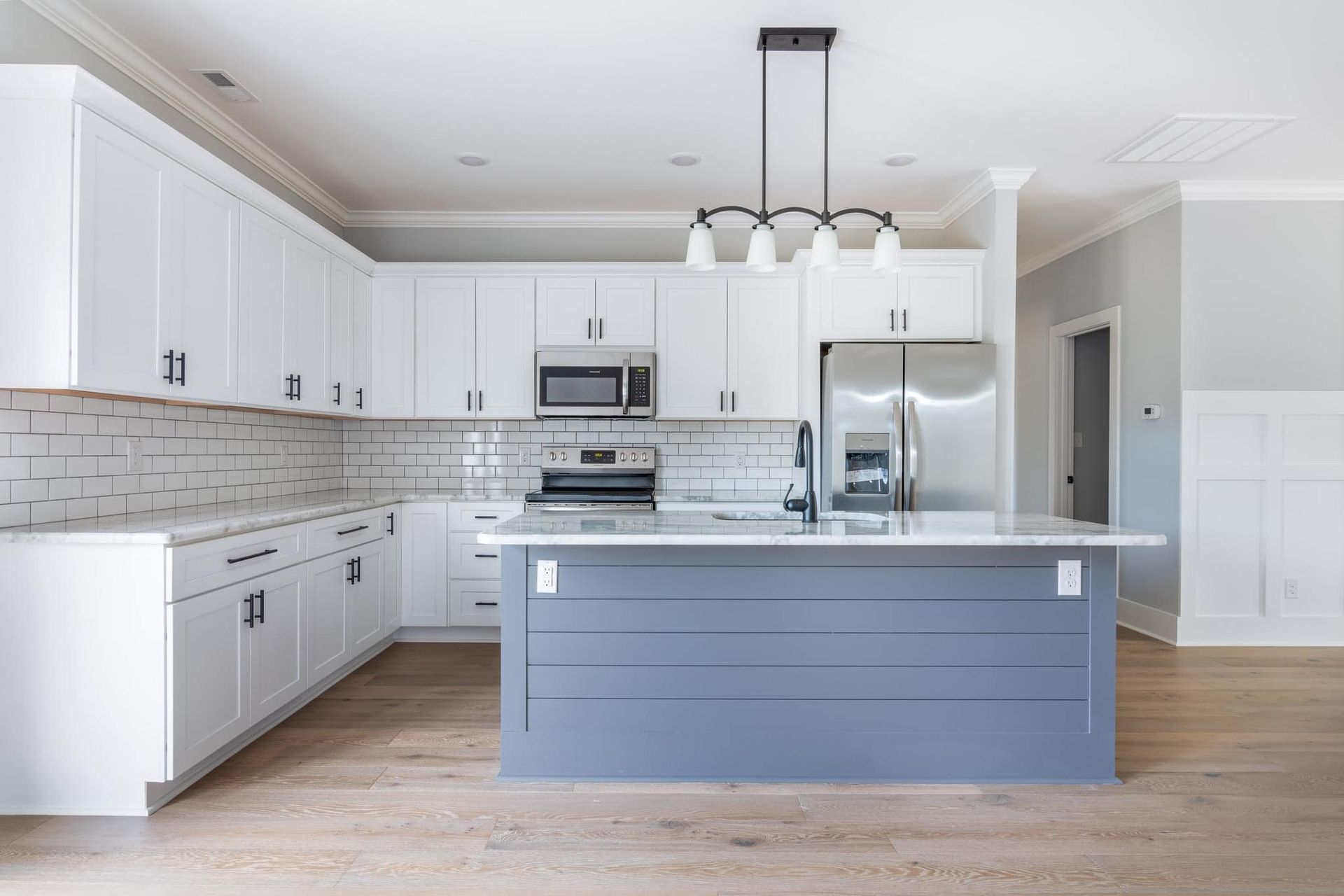 A kitchen with white cabinets , stainless steel appliances , and a large island.