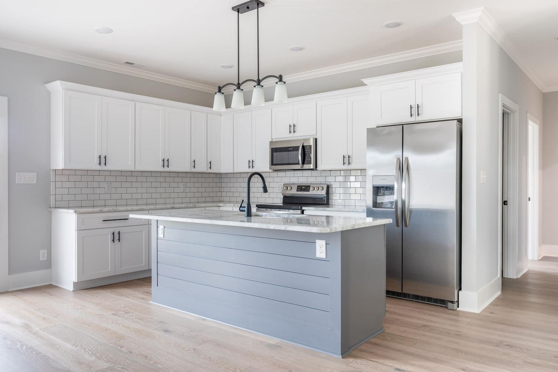 A kitchen with white cabinets , stainless steel appliances , and a large island.