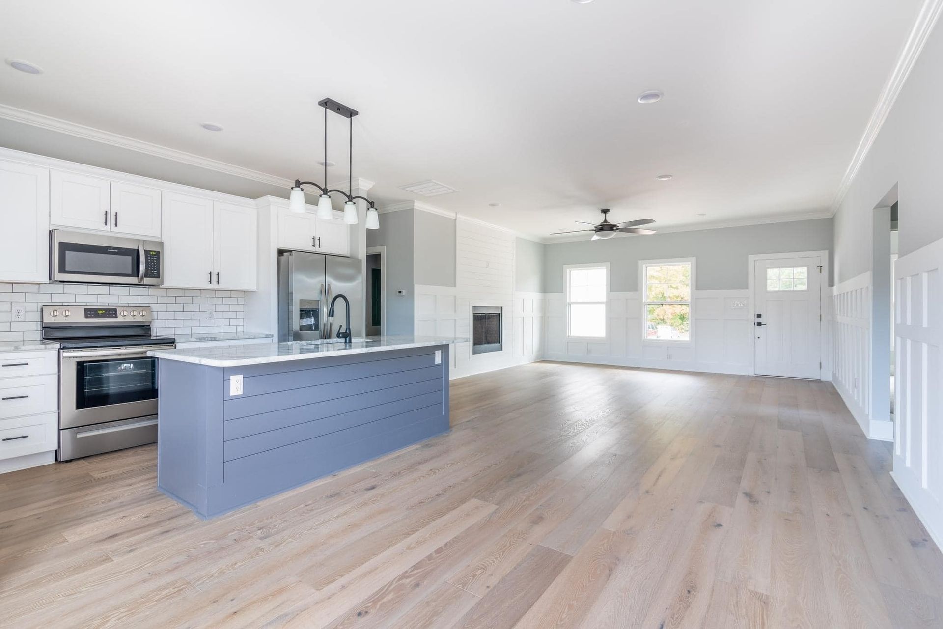 A kitchen with white cabinets , stainless steel appliances , hardwood floors and a large island.