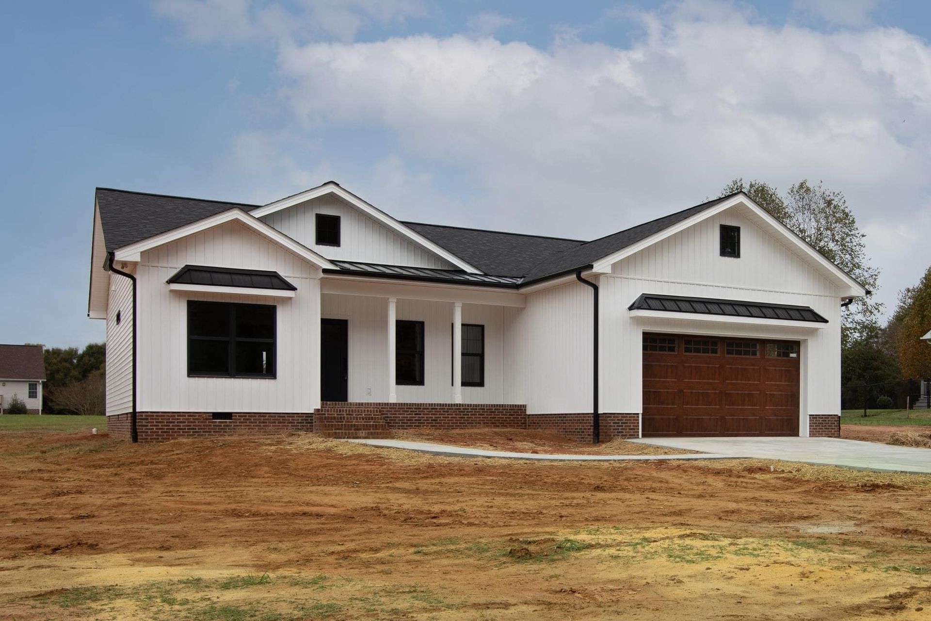 A white house with a black roof is sitting on top of a dirt field.