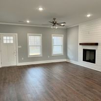 An empty living room with hardwood floors , a fireplace and a ceiling fan.