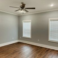 An empty room with a ceiling fan and two windows.