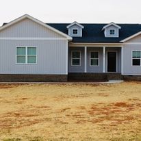 A large white house with a blue roof is sitting on top of a dirt field.