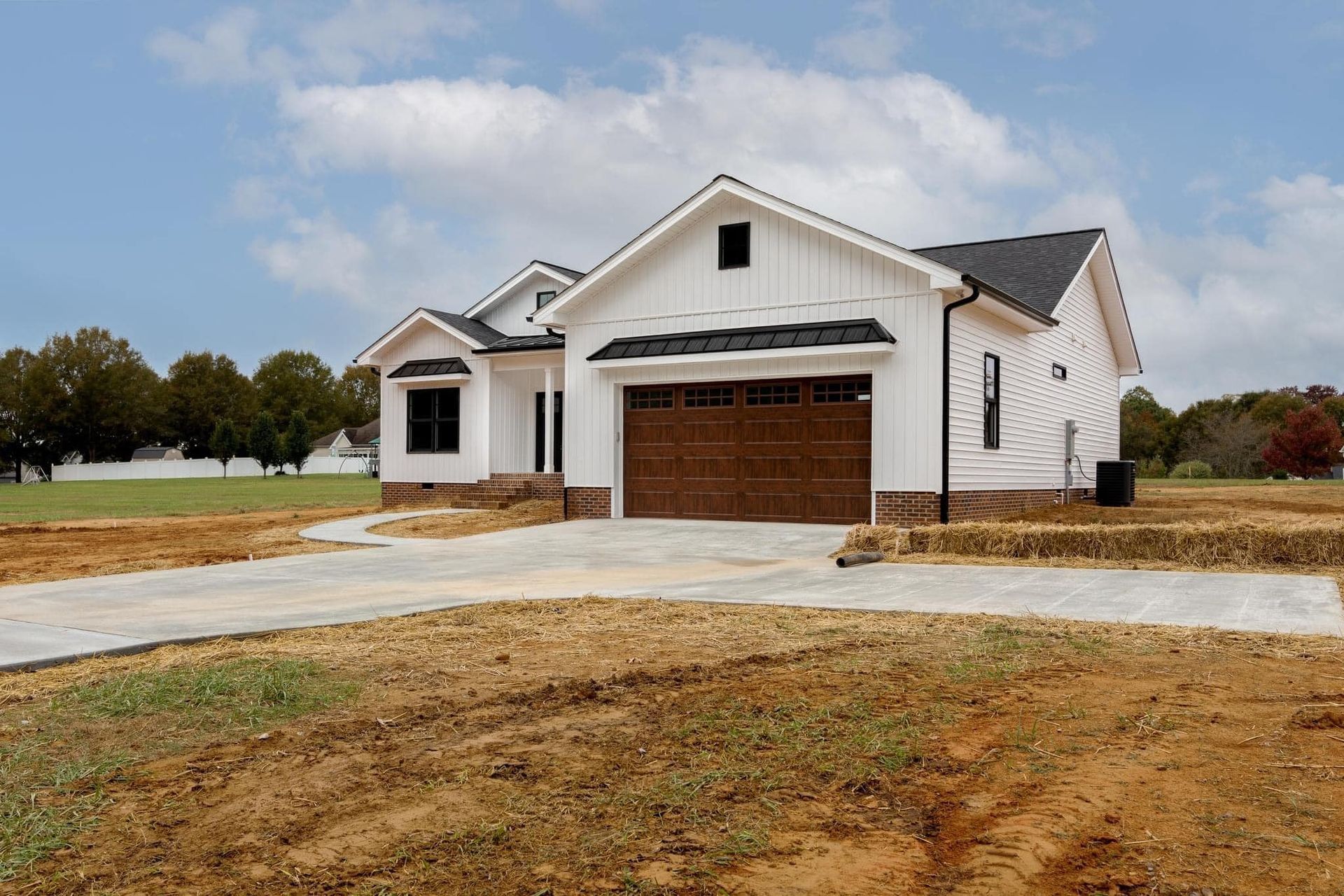 A white house with a brown garage door is sitting on top of a dirt field.