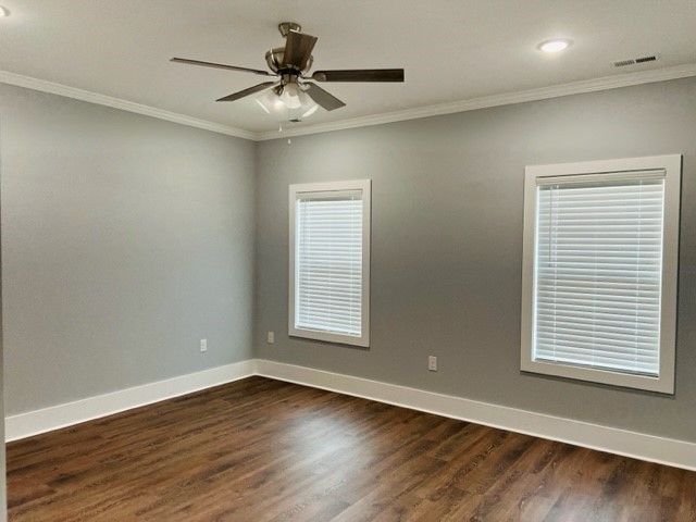 An empty room with a ceiling fan and two windows.