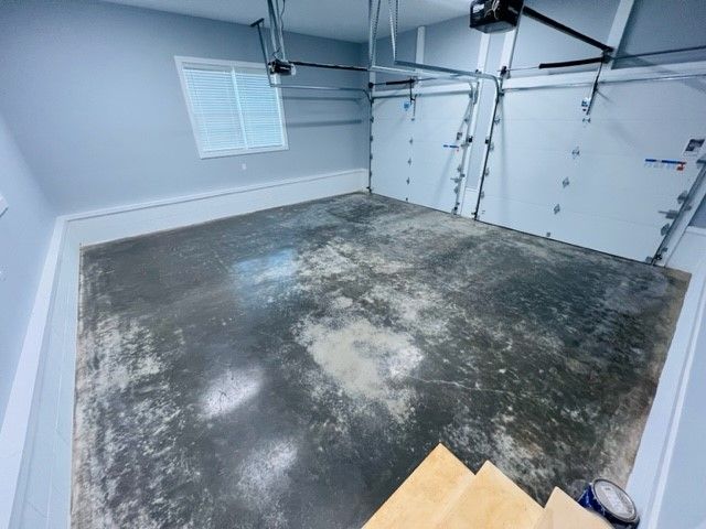 A garage with a concrete floor and a garage door open.