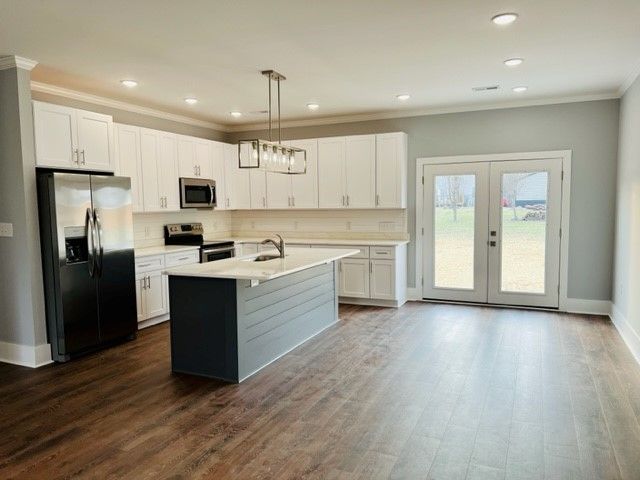 A kitchen with white cabinets , a black refrigerator , and a large island.