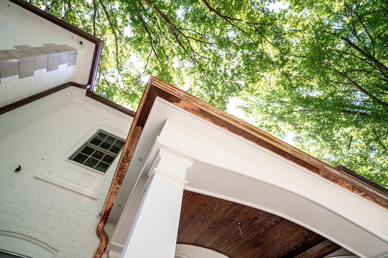 Looking up at the roof of a house with trees in the background.