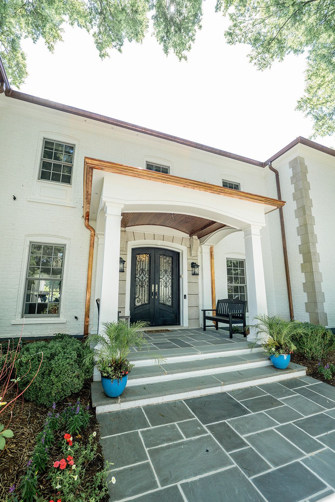 A white house with a black door and a bench in front of it.