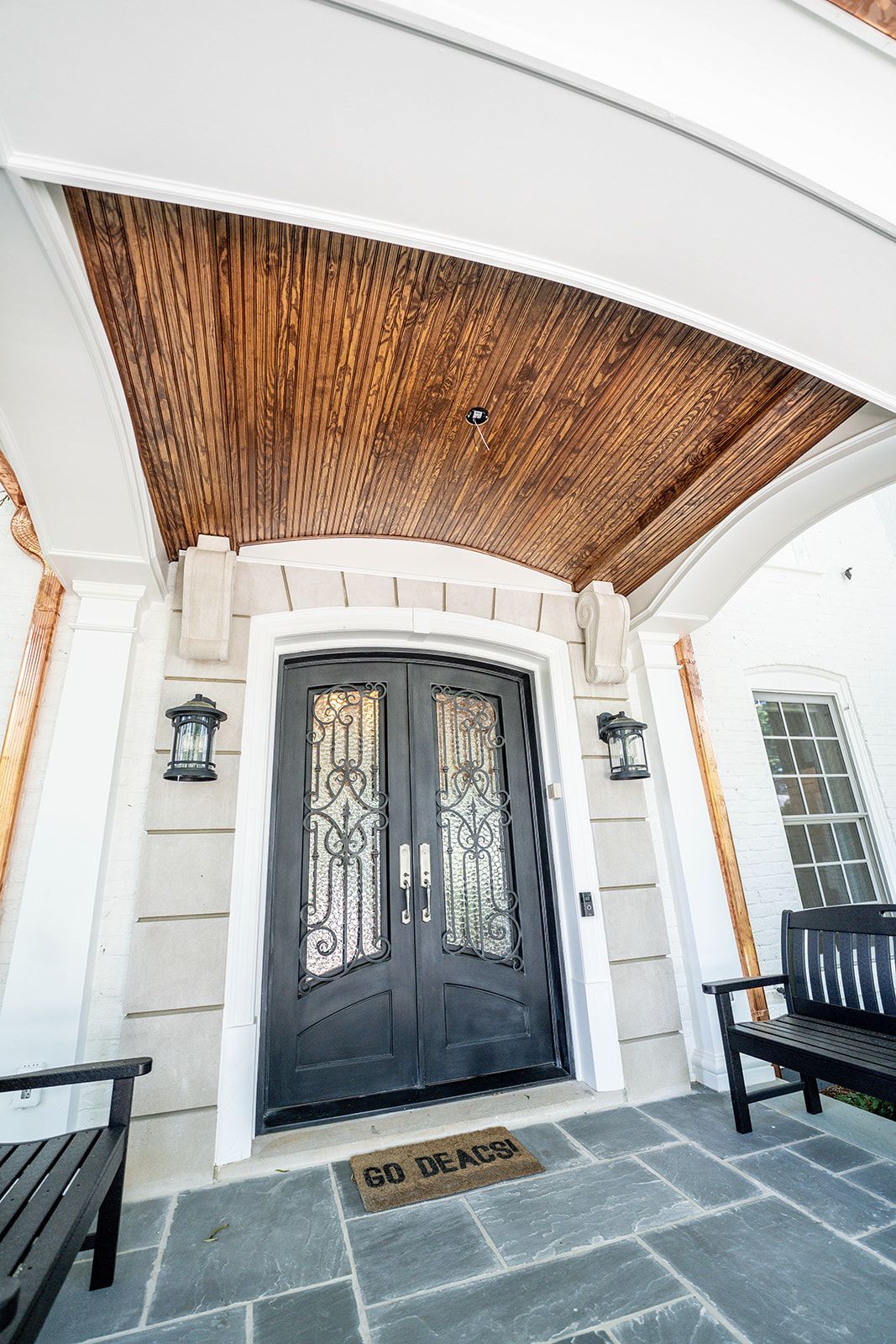 The front door of a house with a wooden ceiling and a bench.