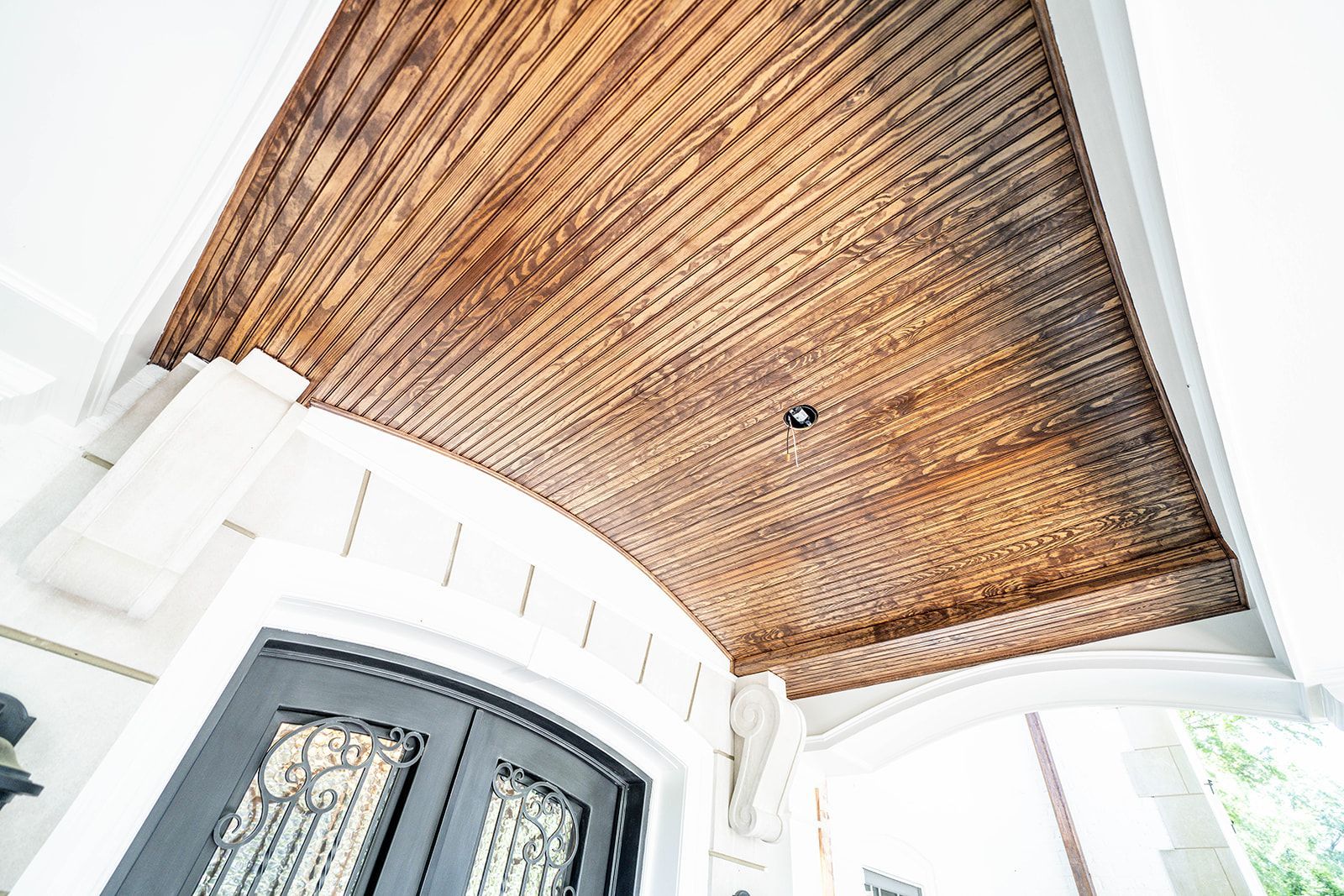A porch with a wooden ceiling and a black door.