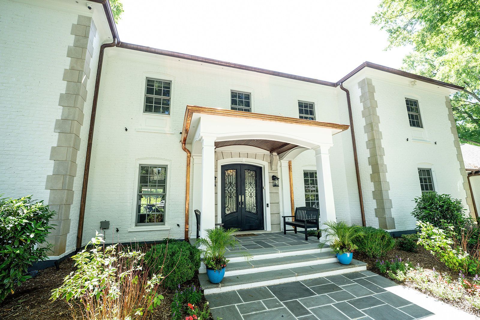 A large white house with a black door and a bench in front of it.