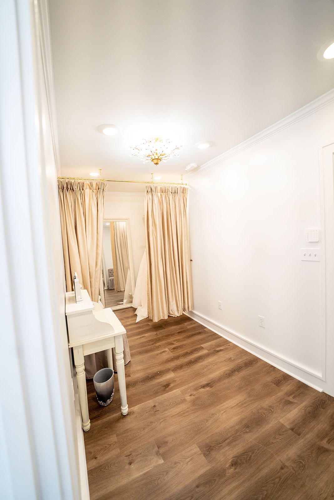 A room with hardwood floors , a table , a mirror and curtains.
