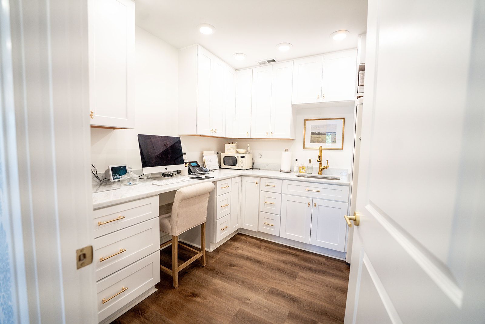 A kitchen with white cabinets and a desk with a computer on it.