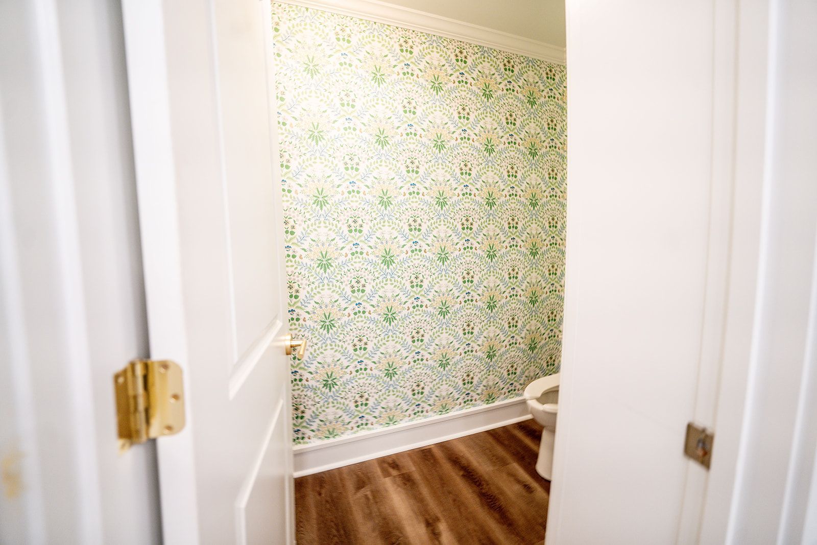 A bathroom with a toilet and floral wallpaper on the wall.