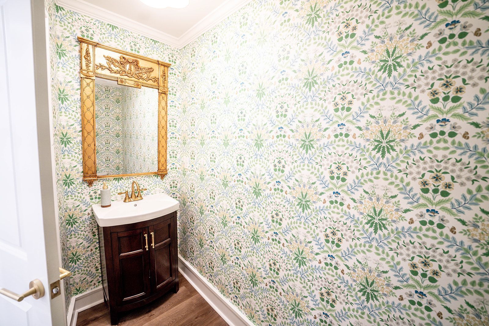 A bathroom with a sink , mirror and floral wallpaper.