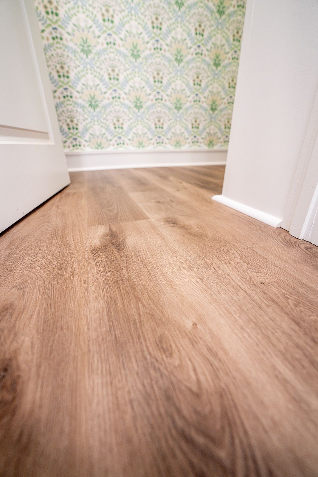 A wooden floor in a hallway next to a door.