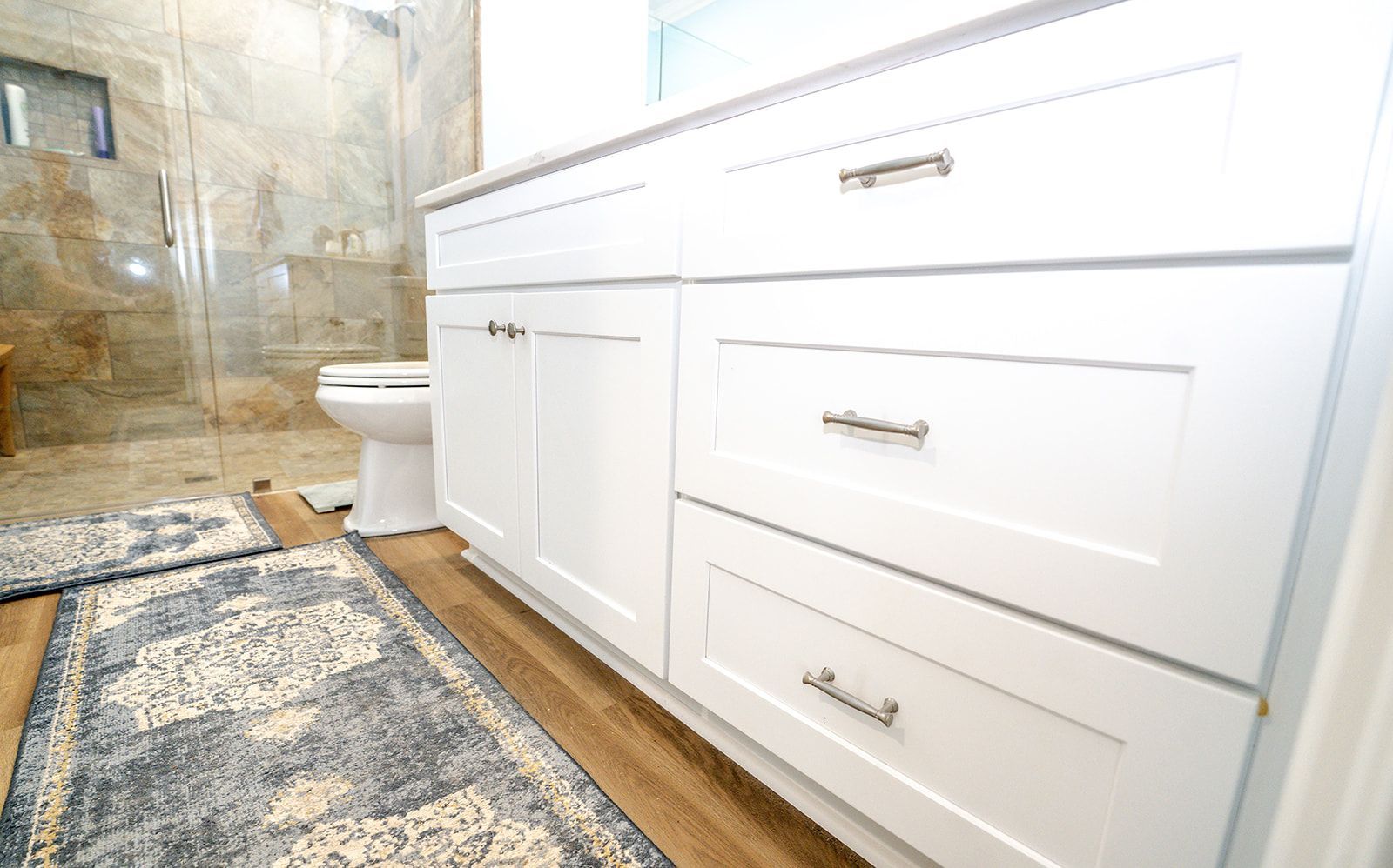 A bathroom with white cabinets , drawers , a toilet and a rug.