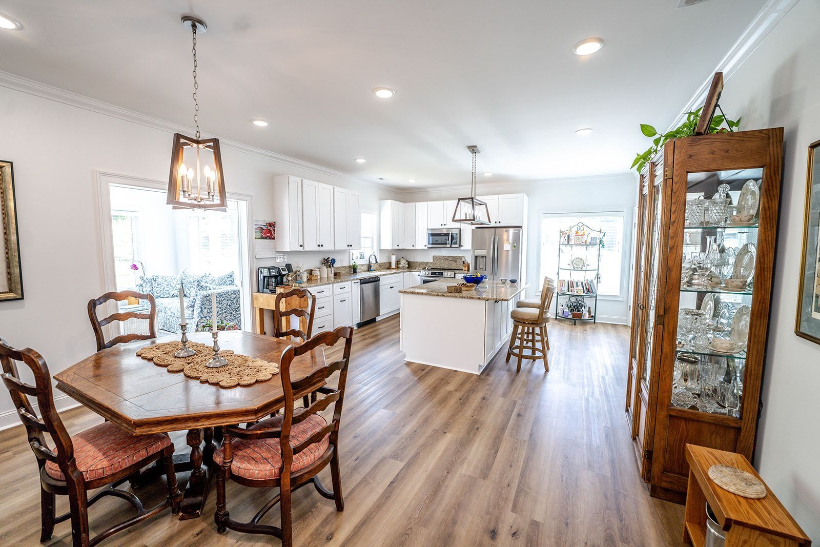 A dining room with a table and chairs and a kitchen in the background.