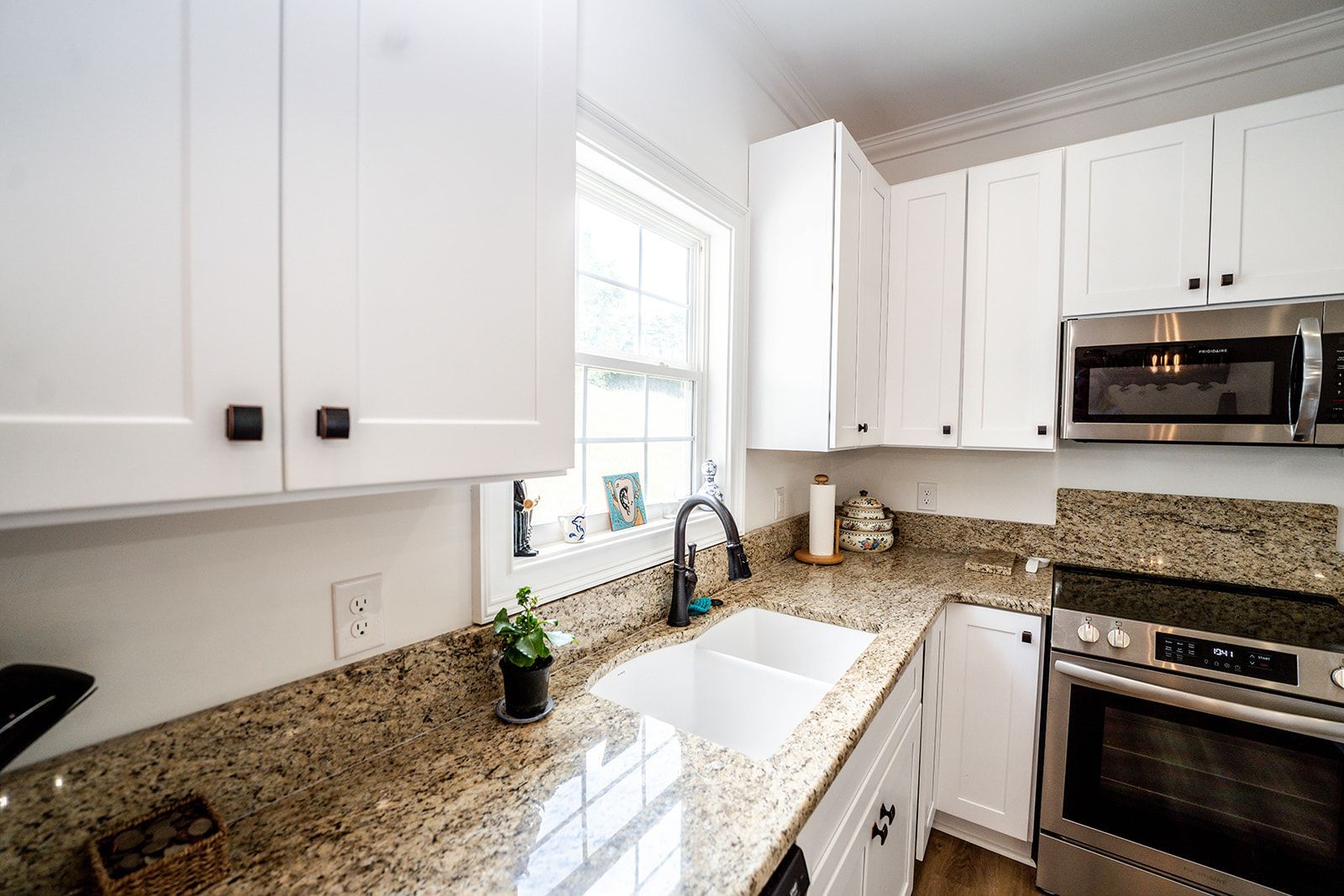 A kitchen with granite counter tops , stainless steel appliances , white cabinets and a window.