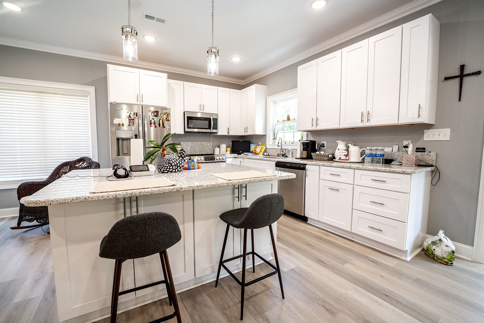 A kitchen with white cabinets and stools and a cross on the wall.