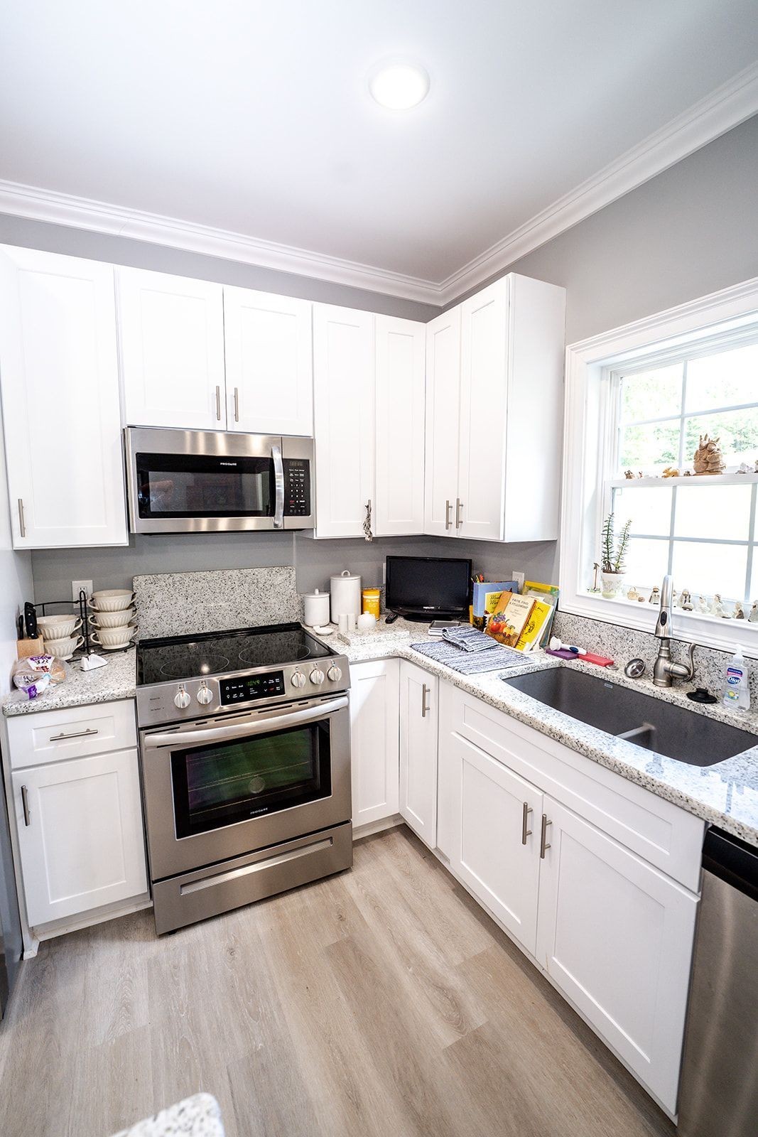 A kitchen with white cabinets , stainless steel appliances , a sink , stove and microwave.