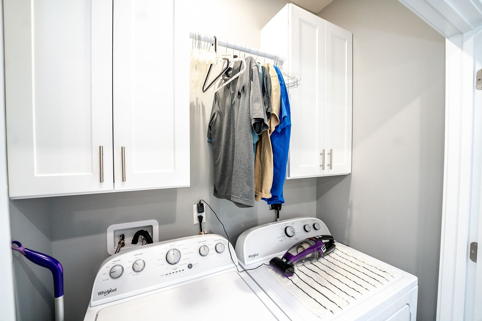A laundry room with a washer and dryer and clothes hanging on the wall.