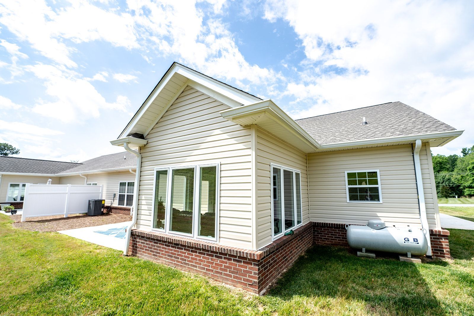A white house with a propane tank in the backyard.
