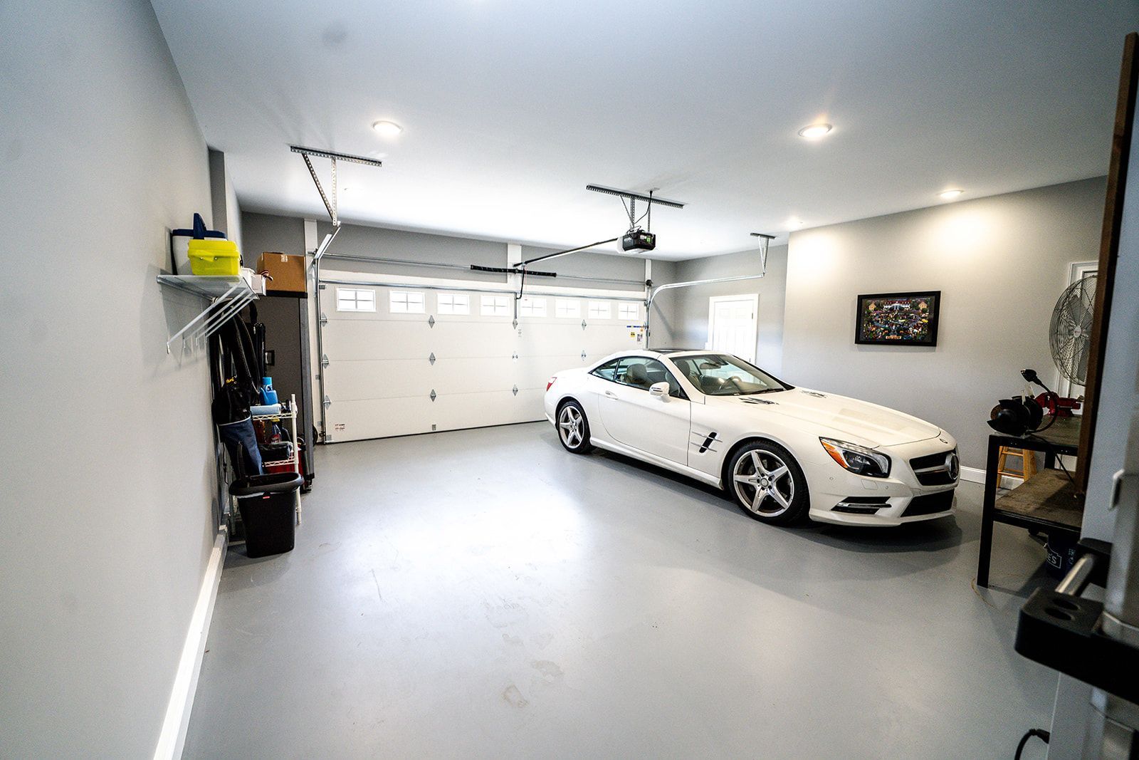 A white sports car is parked in a garage with a garage door open.