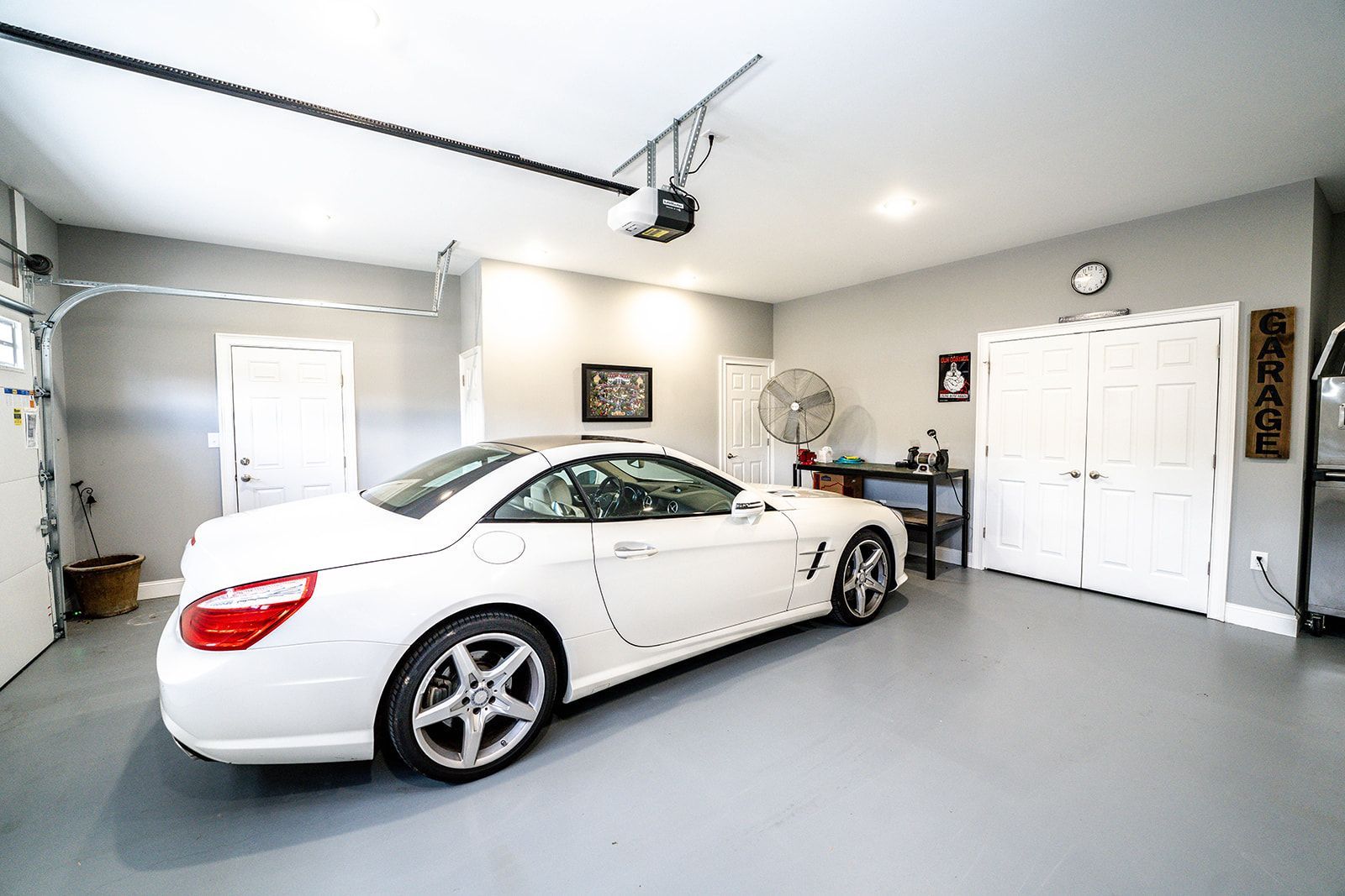 A white sports car is parked in a garage with a garage door open.