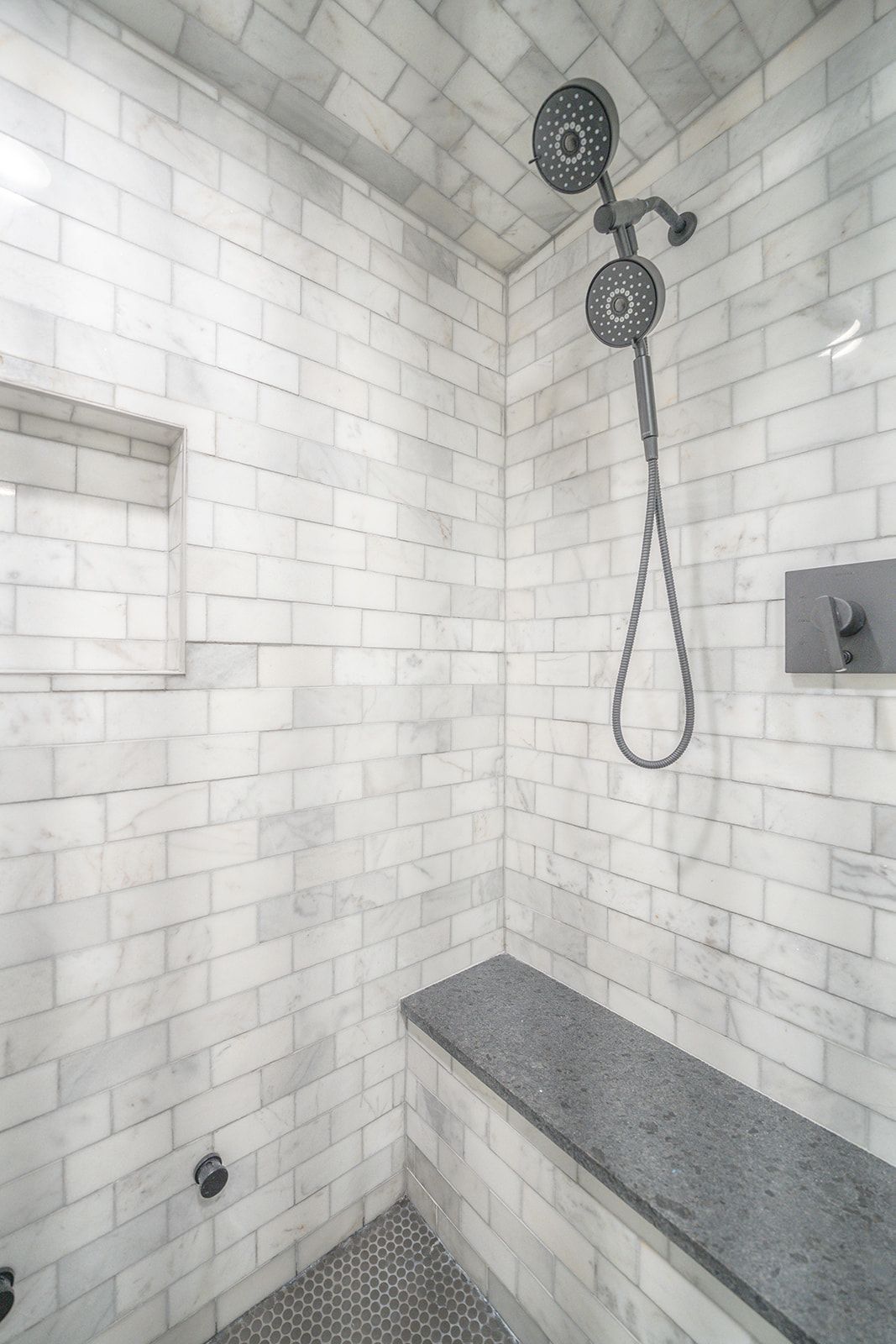 A shower with two shower heads and a bench.